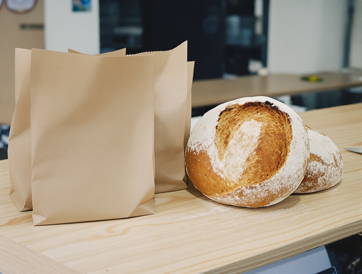 Plain brown paper bread bags beside two flour-dusted round sourdough loaves on a wooden counter