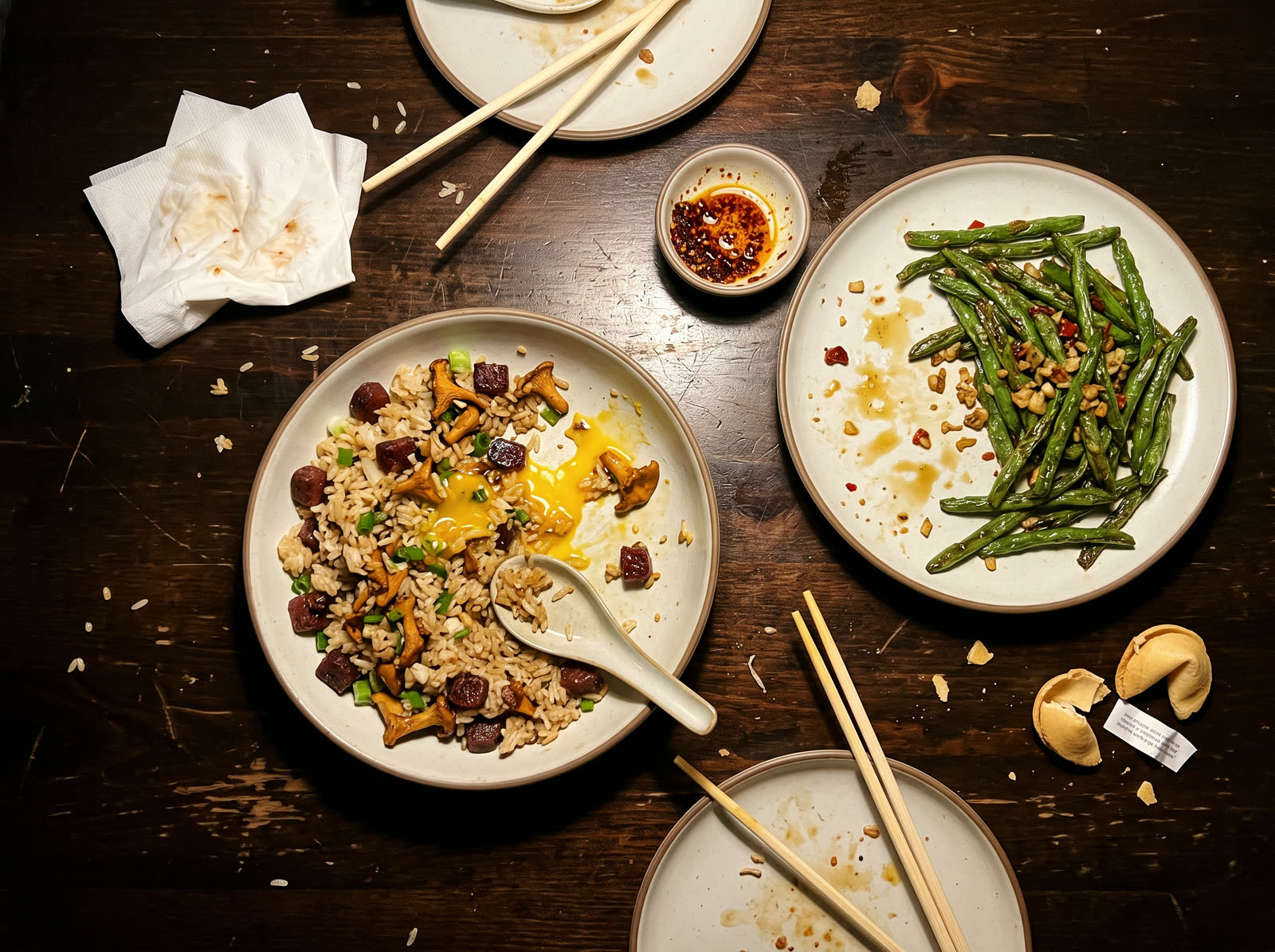 A table after dinner with fried rice, green beans, chopsticks and two cracked fortune cookies